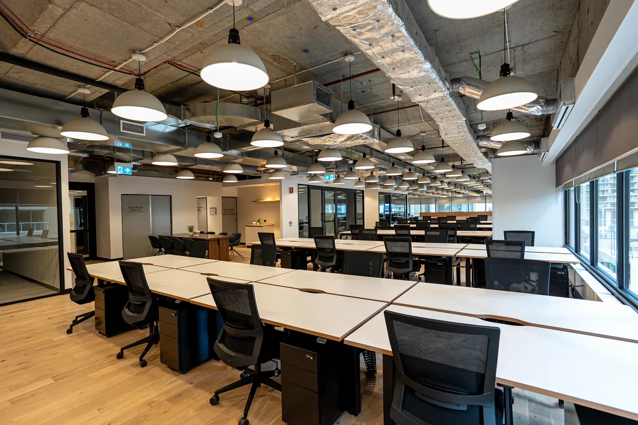 Large open-plan office floor with long workstation runs under pendant lighting