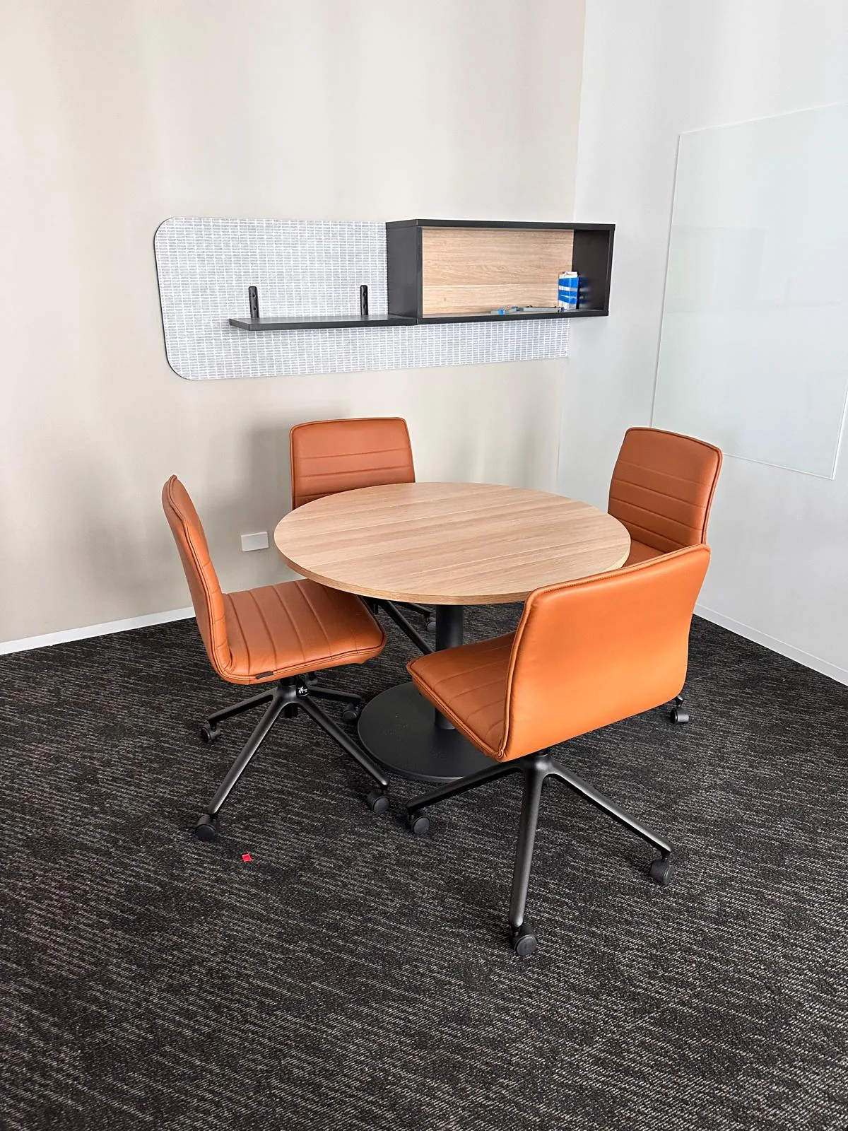 Round meeting table with orange chairs and a wall-mounted shelf