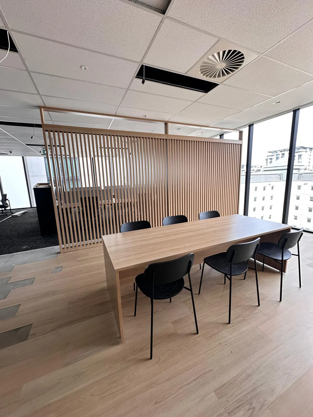 Meeting table in front of a timber slat screen and city windows