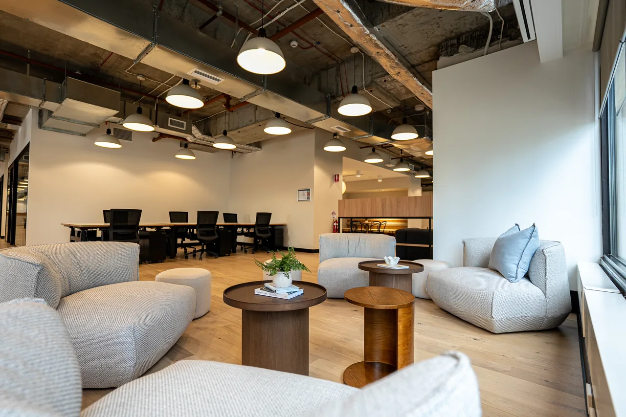 Breakout lounge with modular sofas and timber coffee tables next to open-plan desks